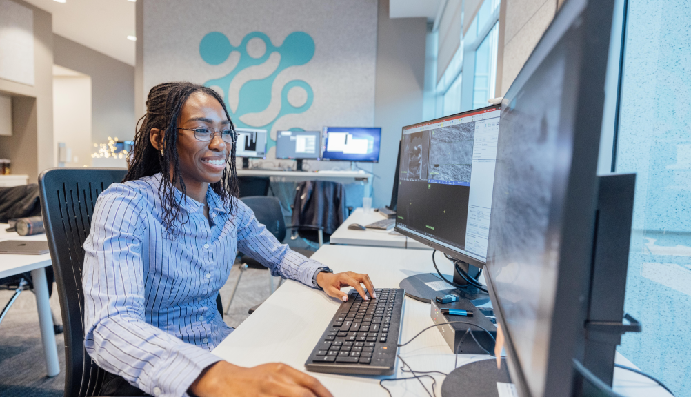 A woman sits at a desk, focused on her computer screen